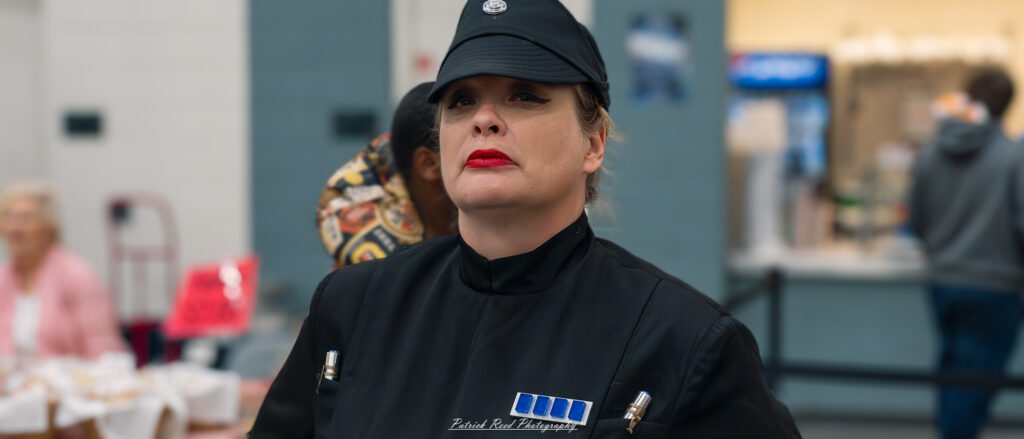 "Cosplayer dressed as a female Imperial Officer from Star Wars, wearing a crisp black uniform with a high collar, gray gloves, and an insignia on the cap, embodying the authoritative and disciplined look of the Galactic Empire."